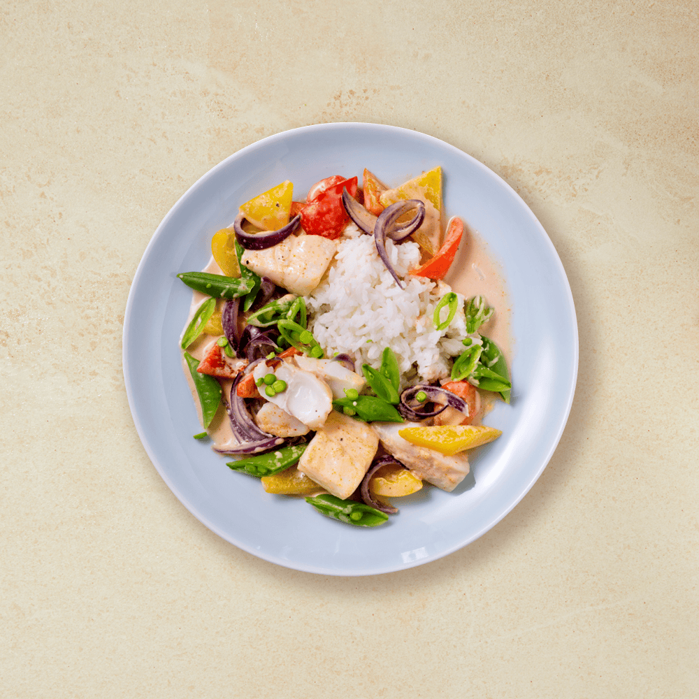 Torsk med kokosmelk, ris og fargerike grønnsaker i en lyseblå skål på beige bakgrunn.