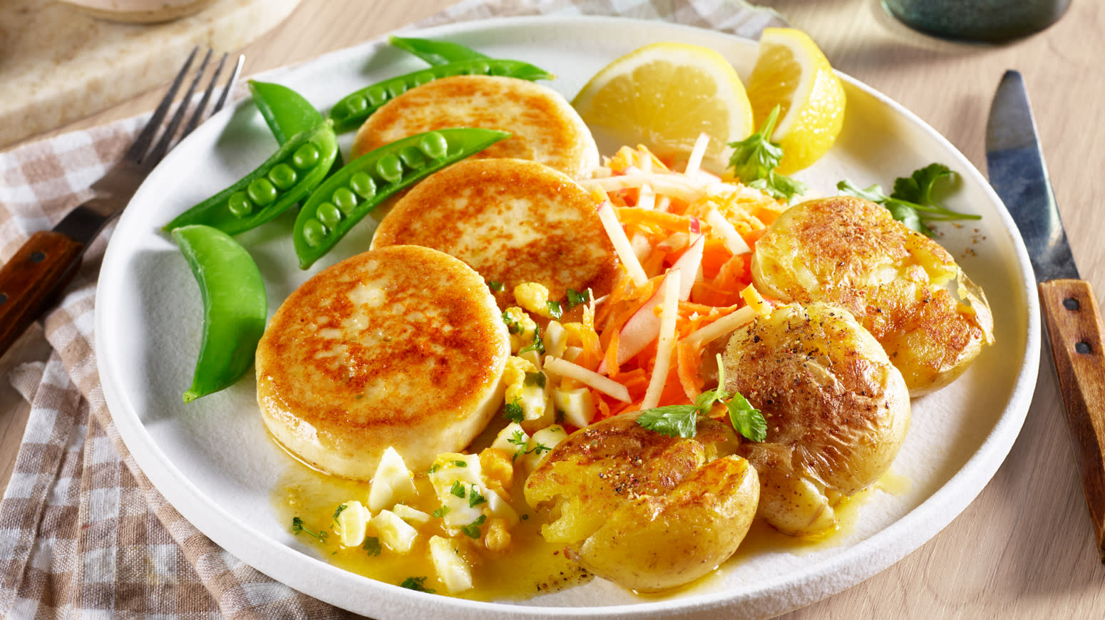 Fiskekaker med råkost og eggsmør servert på hvit tallerken med sitronbåter og sukkererter.