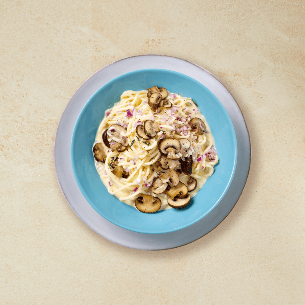 Pasta med kremet sopp, servert i en dyp blå skål som står på en hvit tallerken