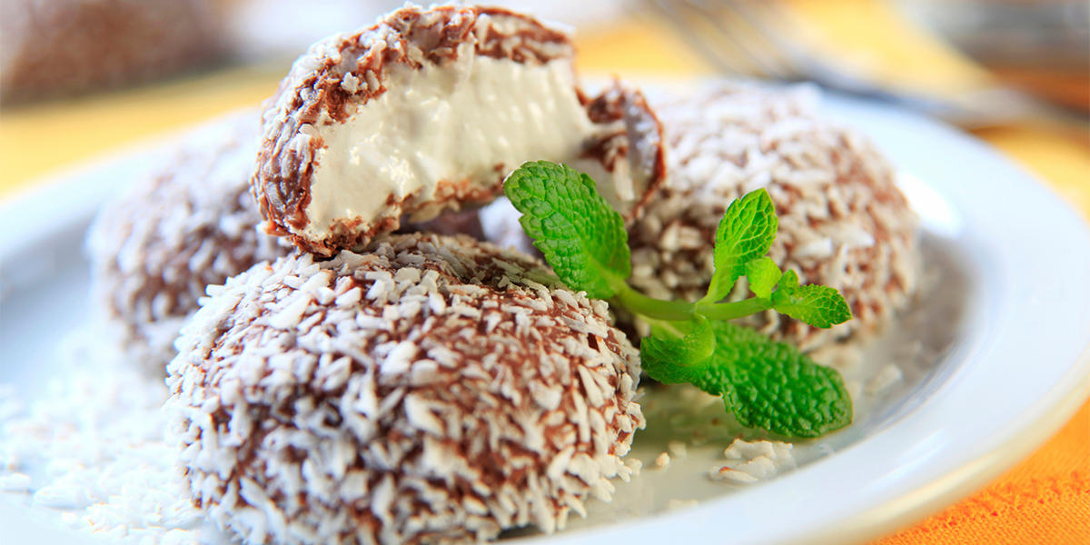 Kokosboller uten sukker servert i tårn på hvit tallerken med et dryss revet kokos og en grønn kvast frisk mynte.