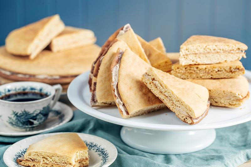 Enkle, tykke lefser med kanelfyll servert på hvitt stettfat på dekket kaffebord. Blåmønstret kaffekopp på siden.