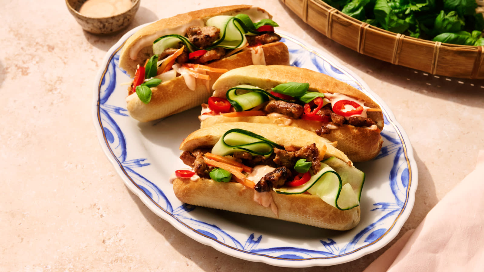 Bánh Mì med strimlet svin servert med syltede grønnsaker på hvit oval asjett med blå mønster.