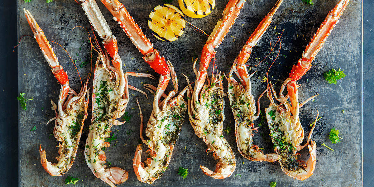 Grillet sjøkreps med hjemmelaget kryddersmør, servert halve på mørkt metallfat med ferske urter og grillet sitron.