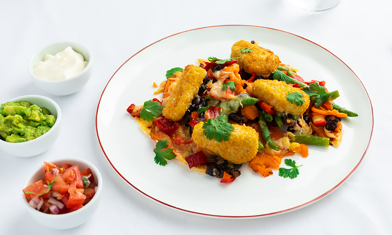 Gratinerte søtpoteter med crispy nuggets, grønnsaker og ost på en hvit tallerken med rød kant.