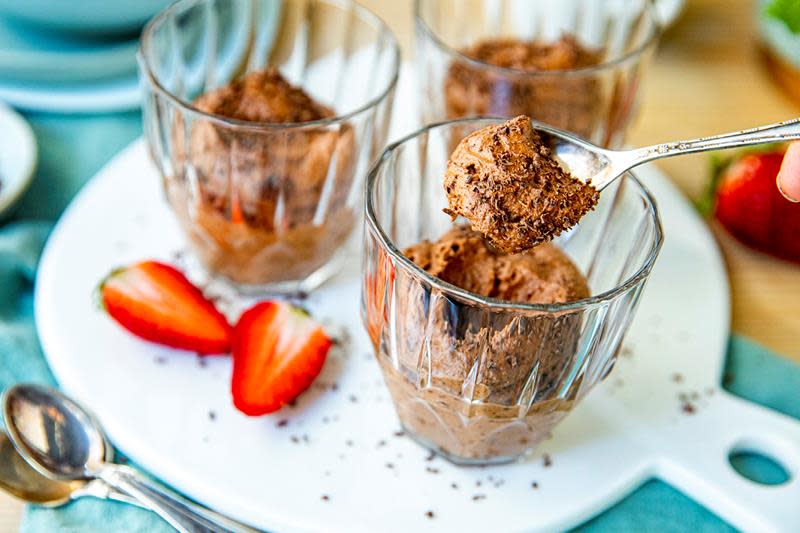 Luftig hjemmelaget sjokolademousse i dessertglass, servert på hvitt rundt fat. Pyntet med revet sjokolade og ferske jordbær. Turkis duk.
