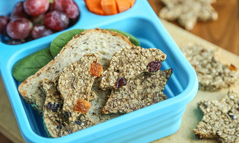 Sunne havrekjeks med banan, formet til biler med tørket frukt som hjul, og lagt i matpakke sammen med brødskiver, druer og gulrot.