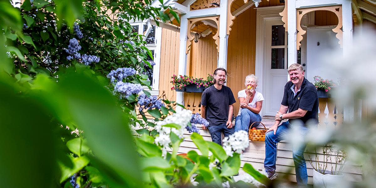Tre mennesker spiser epler på veranda og smiler