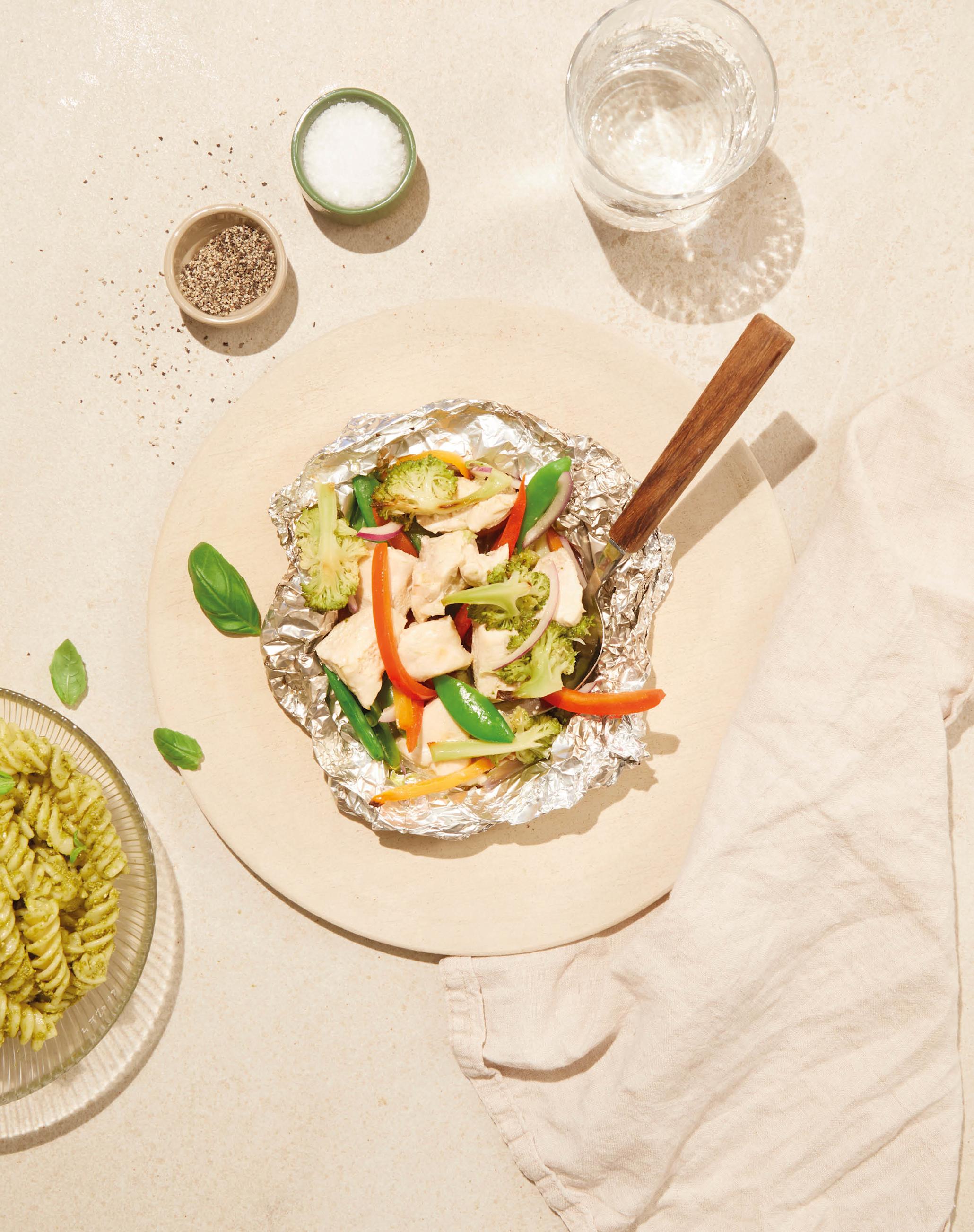 Kyllingfilet i folie med diverse fargerike grønnsaker. Servert på en lys steintallerken.
