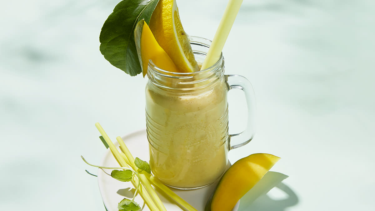 Gul sunn smoothie før trening servert i glasskrus med sugerør og sitronbåter.