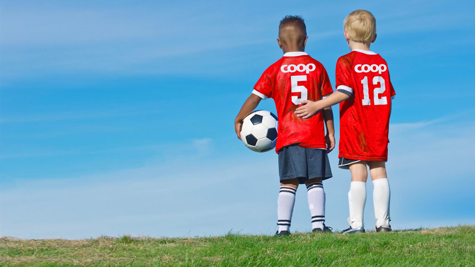 To unge gutter i Coop fotball drakt på åpent landskap