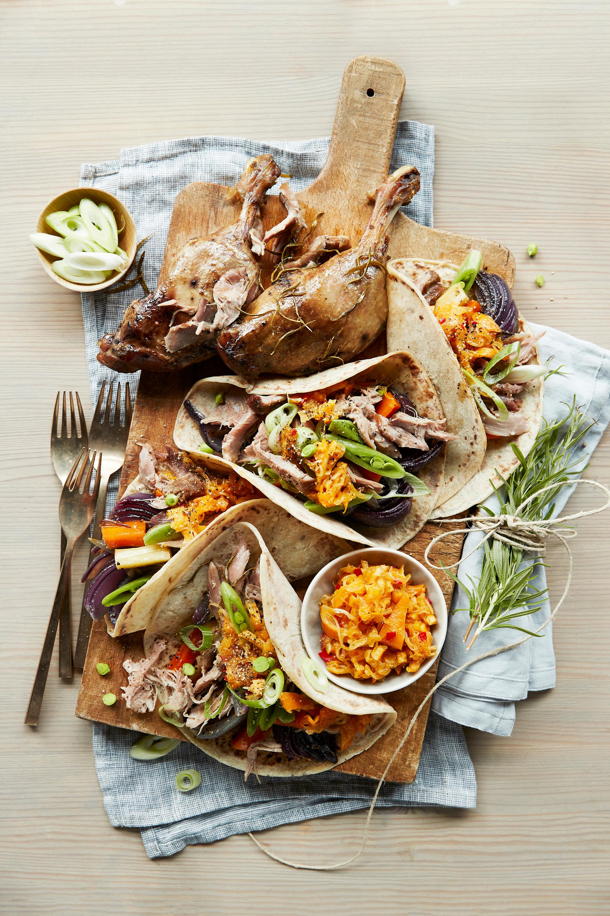 Wraps med andeconfit, ovnsbakte grønnsaker og klementinchutney servert på trefjøl med hele andelår, friske grønnsaker og en liten skål klementinchutney. Gafler ved siden av.