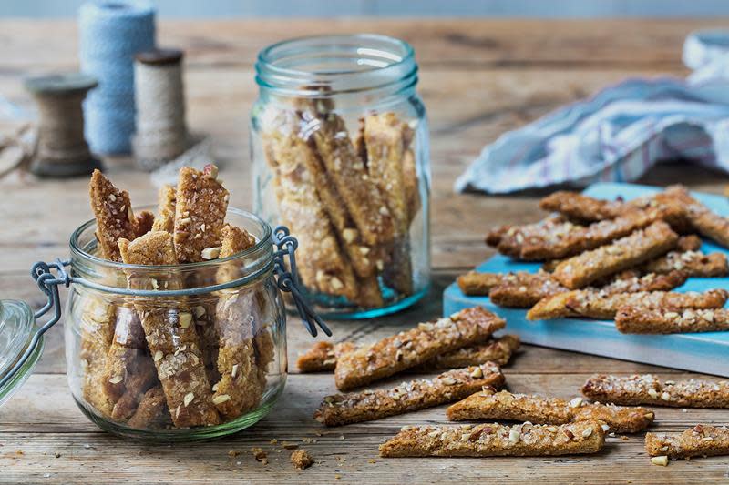 Småkaken Brune pinner lagt i Norgesglass, og servert på rustikk trebord med blått kjøkkenhåndkle.