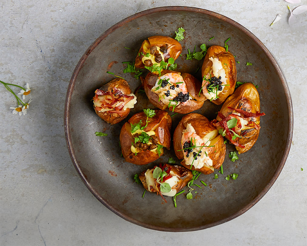 Bakte nypoteter med fyll, på mørk grå tallerken, på lys grå bakgrunn. Potetene er overstrødd med ferske grønne urter.