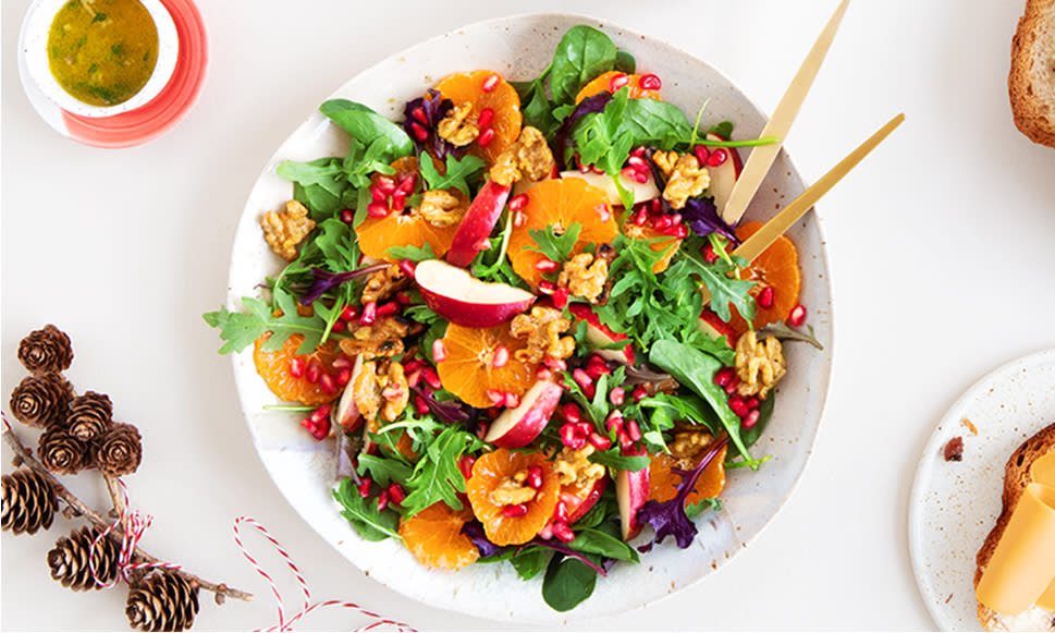 Julesalat med honningristede nøtter, røde epler, klementiner og granateplefrø servert i hvit skål.