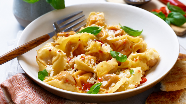  En skål med tortelloni med kryddersmør, revet ost og friske basilikumblader, servert med et stykke hvitløksbrød.