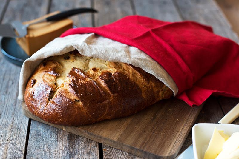 Avlang julekake med rosiner, servert på trefjøl på rustikk trebord, med smør og brunost ved siden av. Linservietter over kaken, i beige og julerødt.