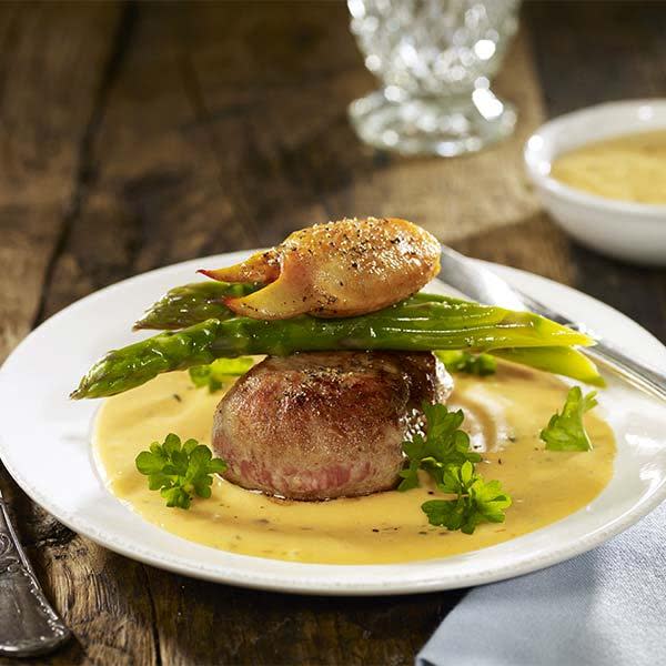 Kalvefilet Oscar dandert på hvit tallerken med asparges og en hummerklo på toppen. Tallerkenen står på mørkt rustikk trebord.