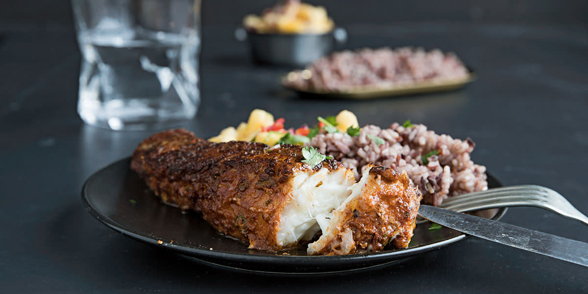 Marinert kveite med eksotisk salsa servert på mørk tallerken med villris til, på mørkt bord. Lite fat med villris og skål med eksotisk salsa i bakgrunnen.