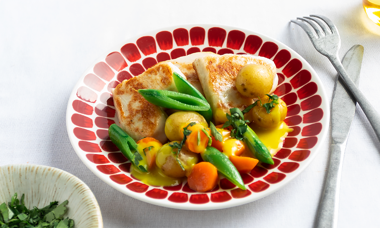 Hjerteformede fiskekaker på rødmønstret tallerken, sammen med poteter, gulrot, sukkererter og hvit saus med karri.