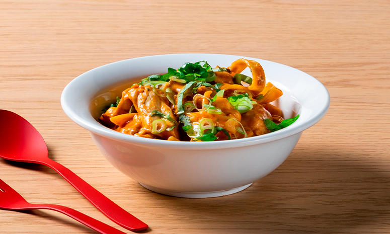 Spansk kyllinggryte med tagliatelle servert i en dyp hvit skål med rødt bestikk liggende på venstre side