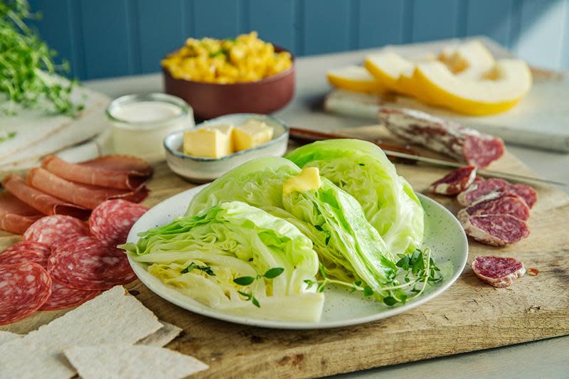 Knallgrønn smørdampet sommerkål, toppet med en klatt smør. Servert på et trebord med spekemat, melon, eggerøre, flatbrød og ferske urter.