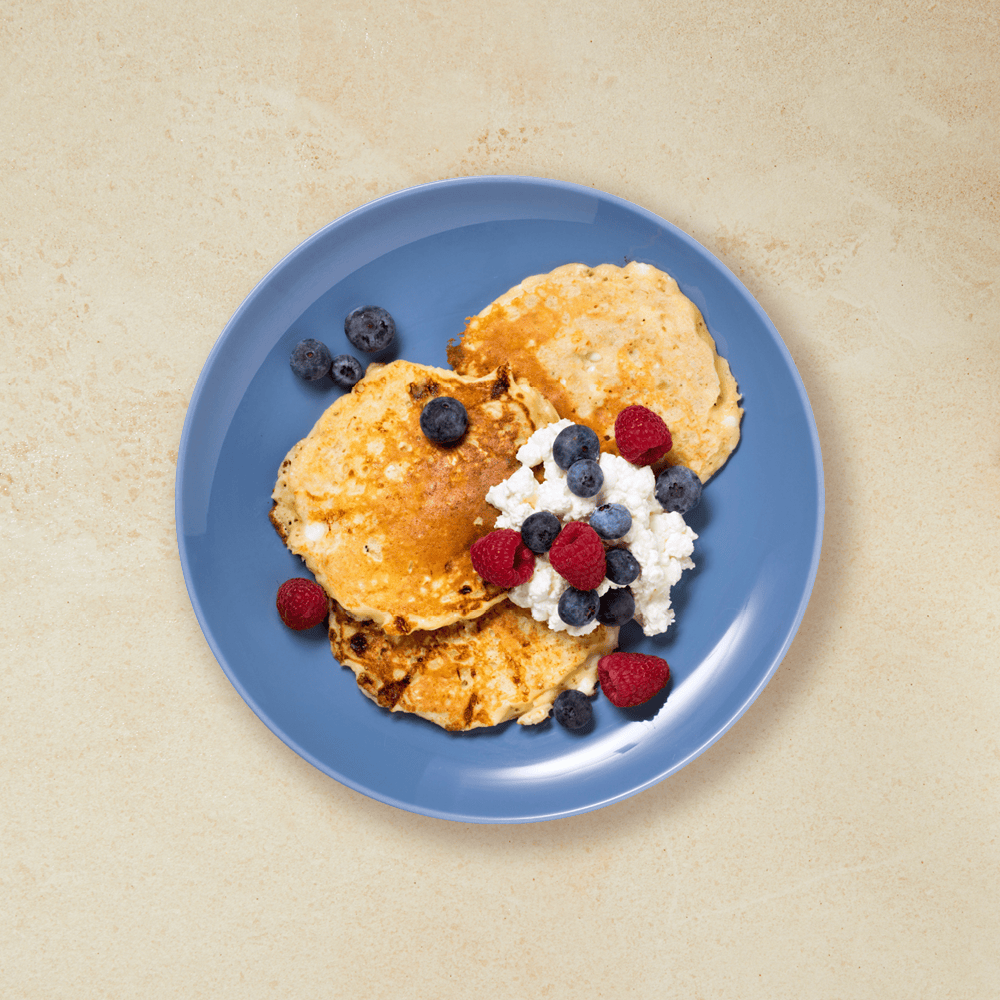 Proteinpannekaker med cottage cheese, blåbær og bringebær, alt ligger på en blå tallerken