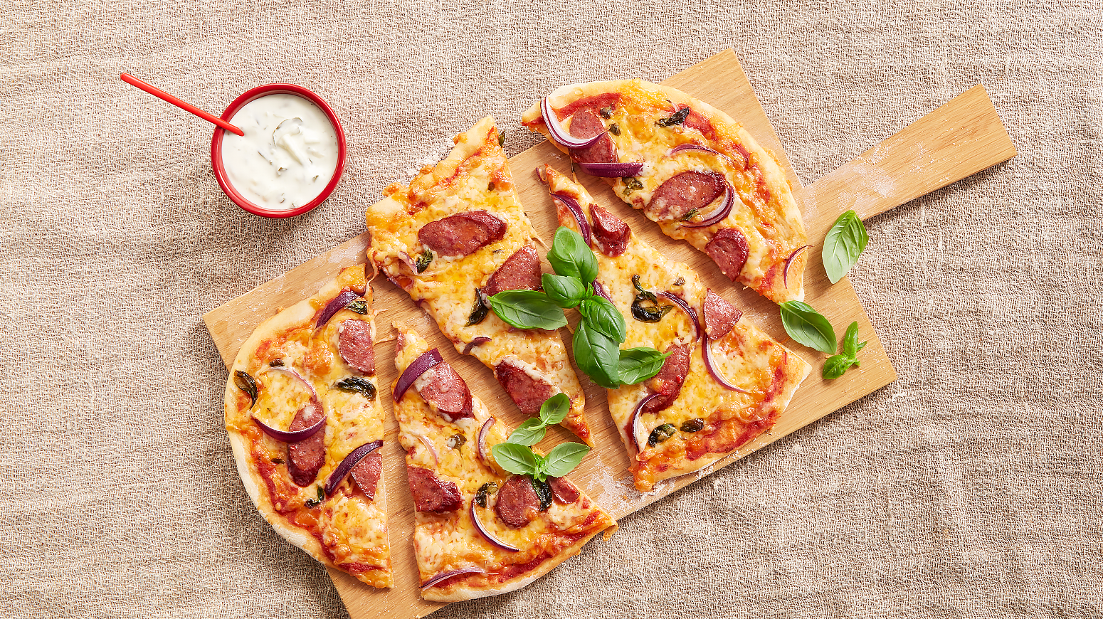 Pizza med chorizo style pølse og cheddar, rødløk og fersk basilikum. Servert på lys trefjøl.