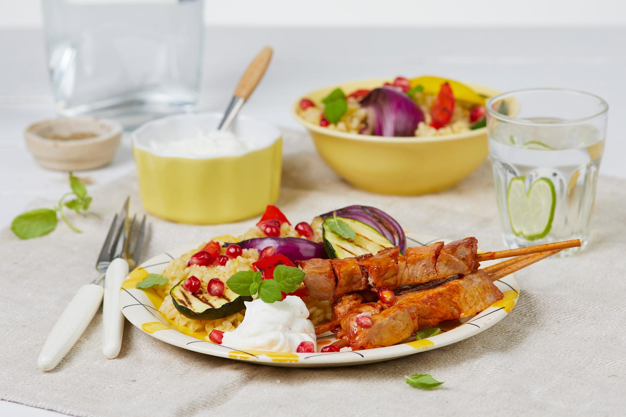 Grillspyd BBQ svin med bulgursalat og yoghurt-dipp på en hvit og gul tallerken med en gul skål med yoghurtdipp og en gul skål med bulgursalat bak
