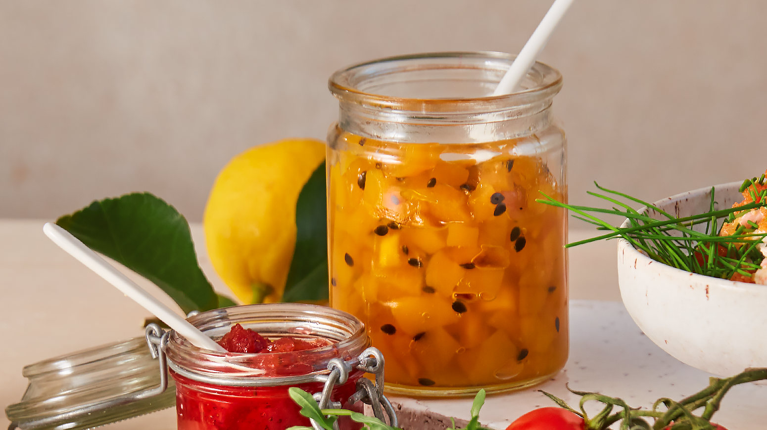 Syltetøy med solmoden mango og pasjonsfrukt i gjennomsiktig krukke på frokostbord.