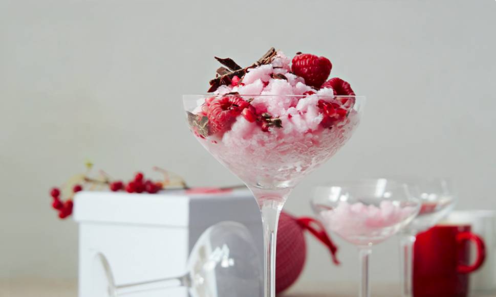 Julebrus -sorbet servert i høye glass, pyntet med sjokolade, bringebær og granateple på middagsbord med stettglass og hvit gaveeske.