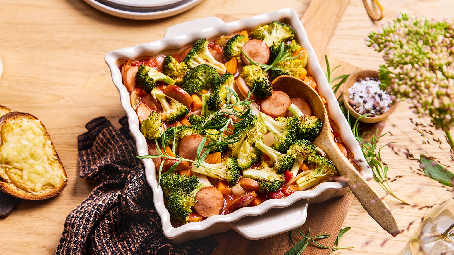 Pølseform med ris og tomat servert i hvit ildfast form med ostesmørbrød ved siden av.