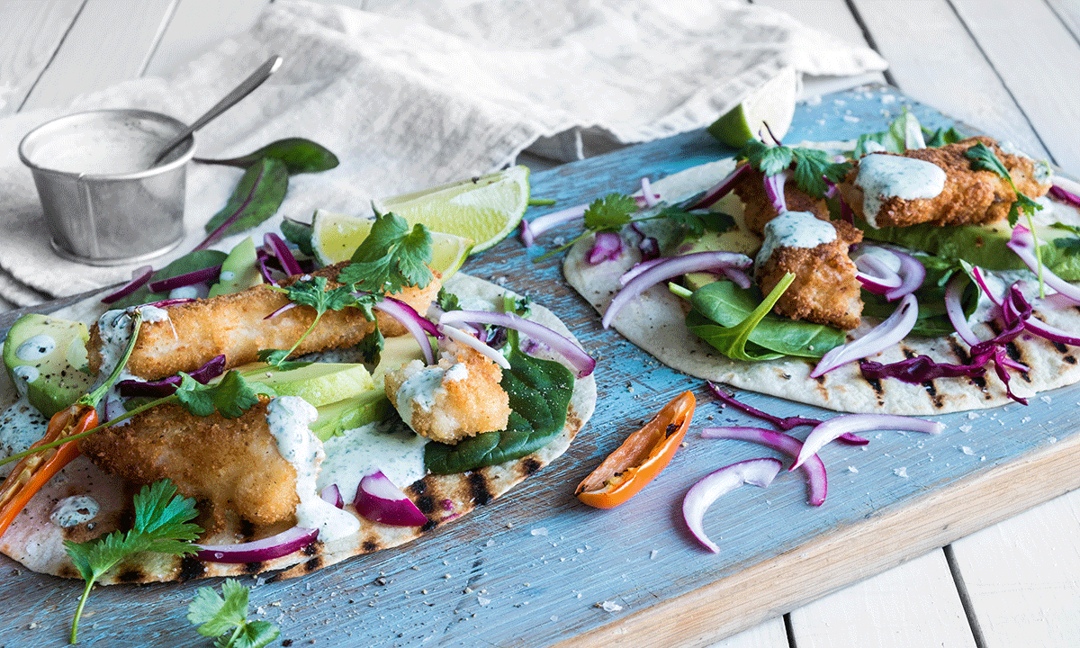 Taco med sprøstekt torsk, servert i lomper, med limekrem, koriander, salat og rødløk.