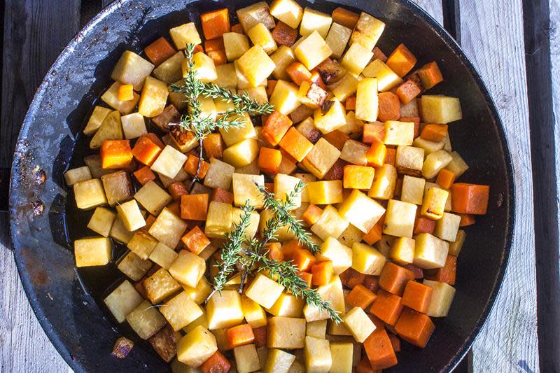 Fargerike rotgrønnsaker delt i terninger, stekes i svart støpejernspanne med ferske timiankvister på toppen.