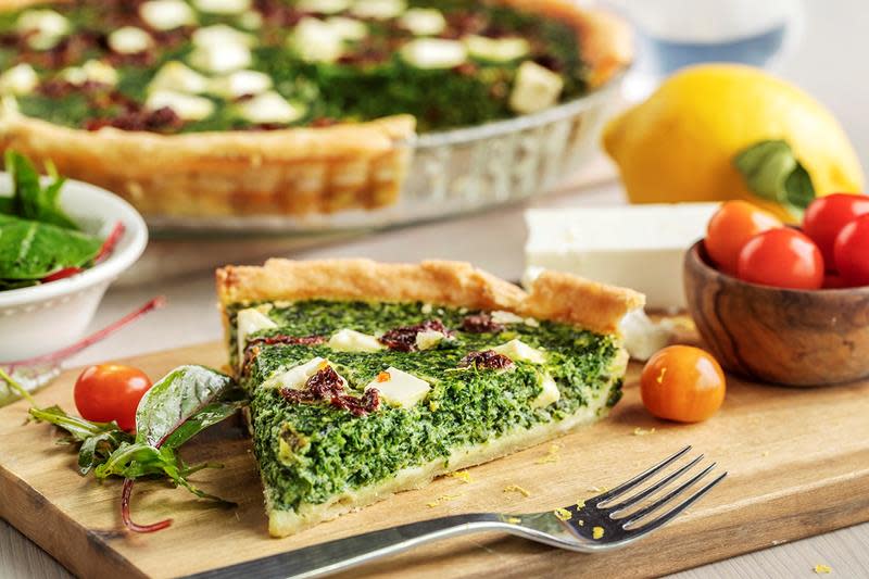 Pai med fetaost, spinat og soltørkede tomater, servert på trefjøl med fargerike ferske tomater. Sitron i bakgurnnen.