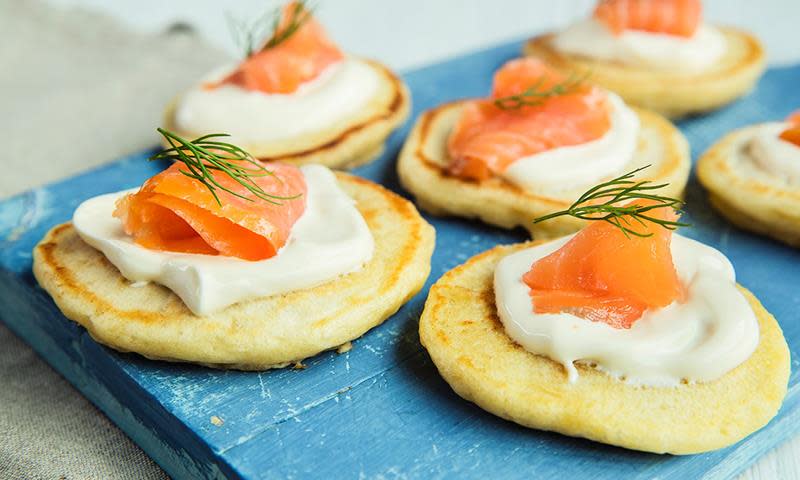 Luftige blinis med røkelaks, creme fraiche og frisk dill servert på blå trefjøl.