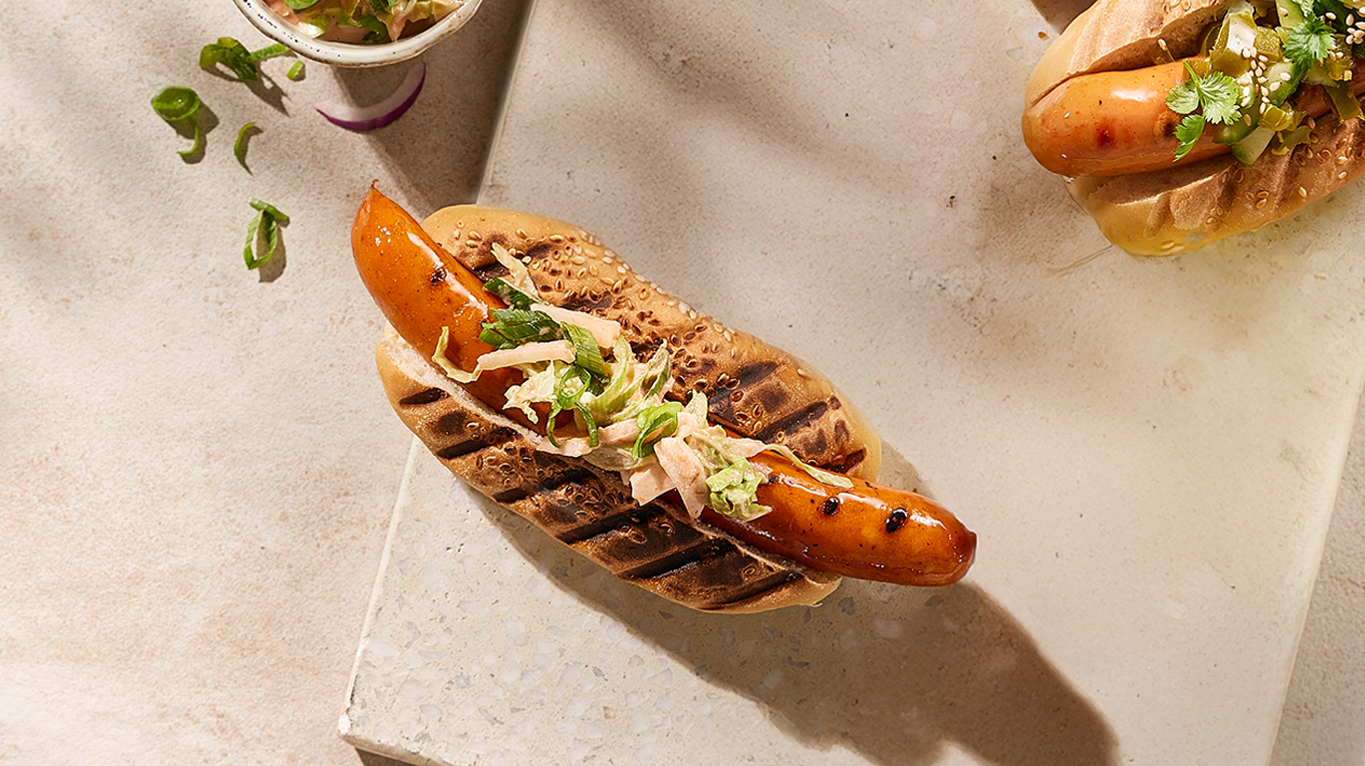 Spicy chicken pølse med kimchi-slaw servert i pølsebrød på lys marmorfjøl.