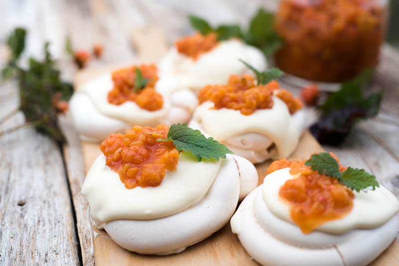 Minipavlova med multer og pisket krem, servert på lys trefjøl på rustikk trebord. Glass med multer i bakgrunnen.