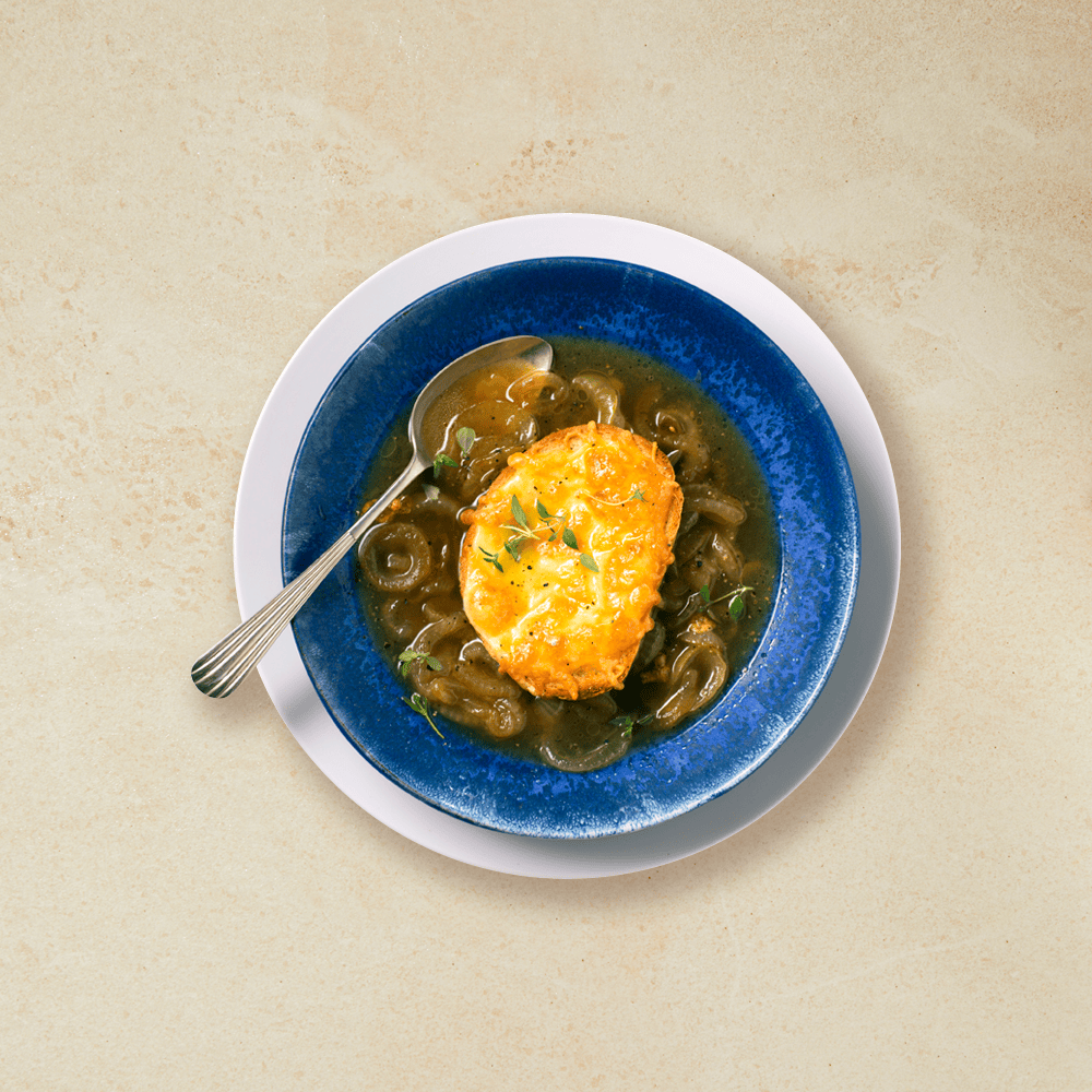 Løksuppe med ostebrød, servert i en mørk blå skål med en skje på vestre siden