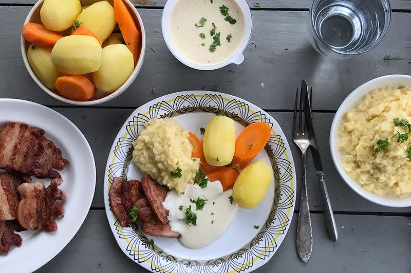 Flesk og duppe servert på lys middagstallerken, servert med kålrotmos, kokte poteter og gulrot. Mørk grå bakgrunn.