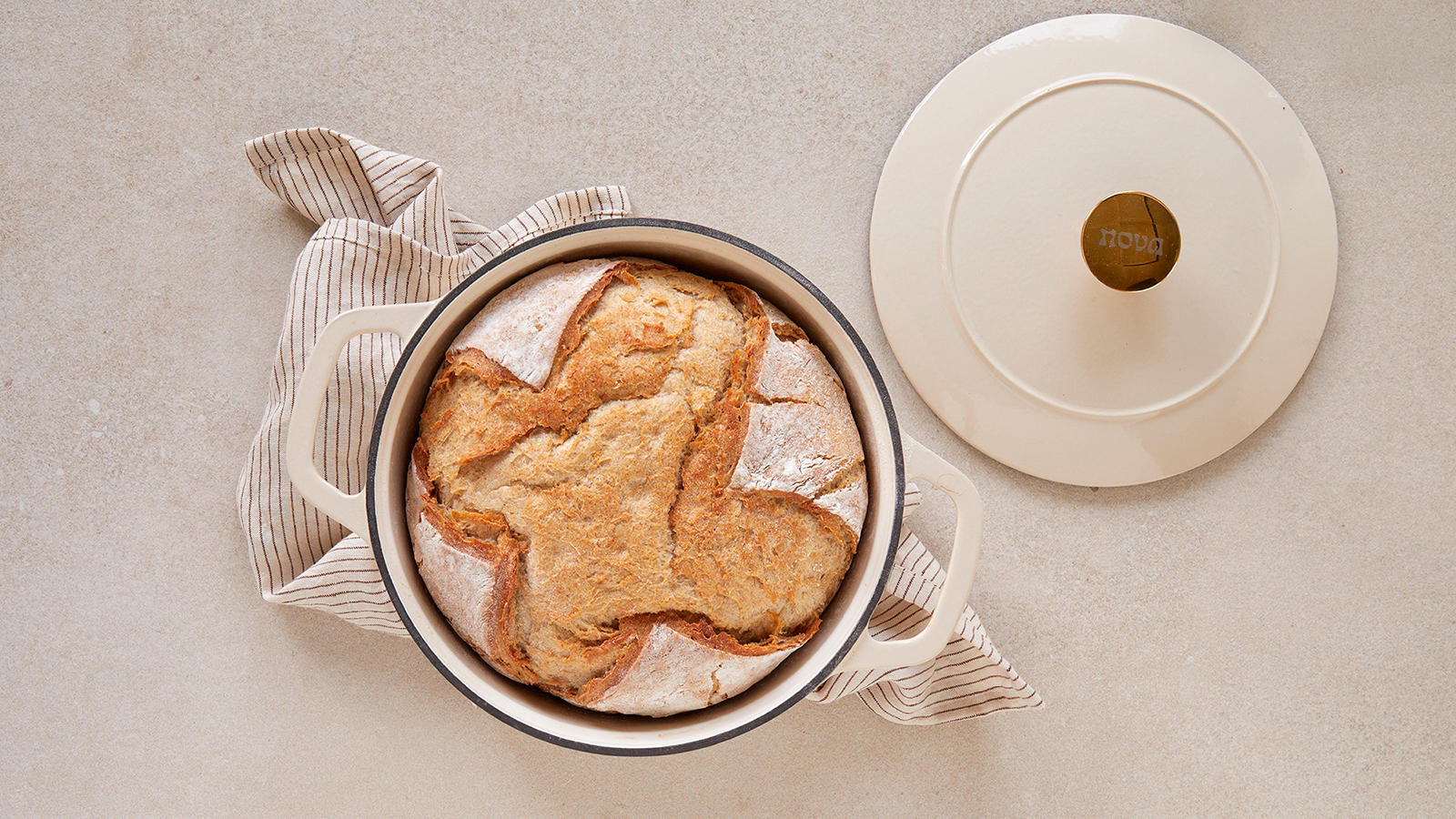 Luftig grytebrød med sprø skorpe bakt og servert i hvit støpejernsgryte på hvitt og beige kjøkkenhåndkle.