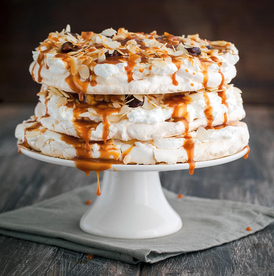 Pavlova i flere lag, med krem, skivede mandler og salt karamell ringlet over. Servert på hvitt stettfat.
