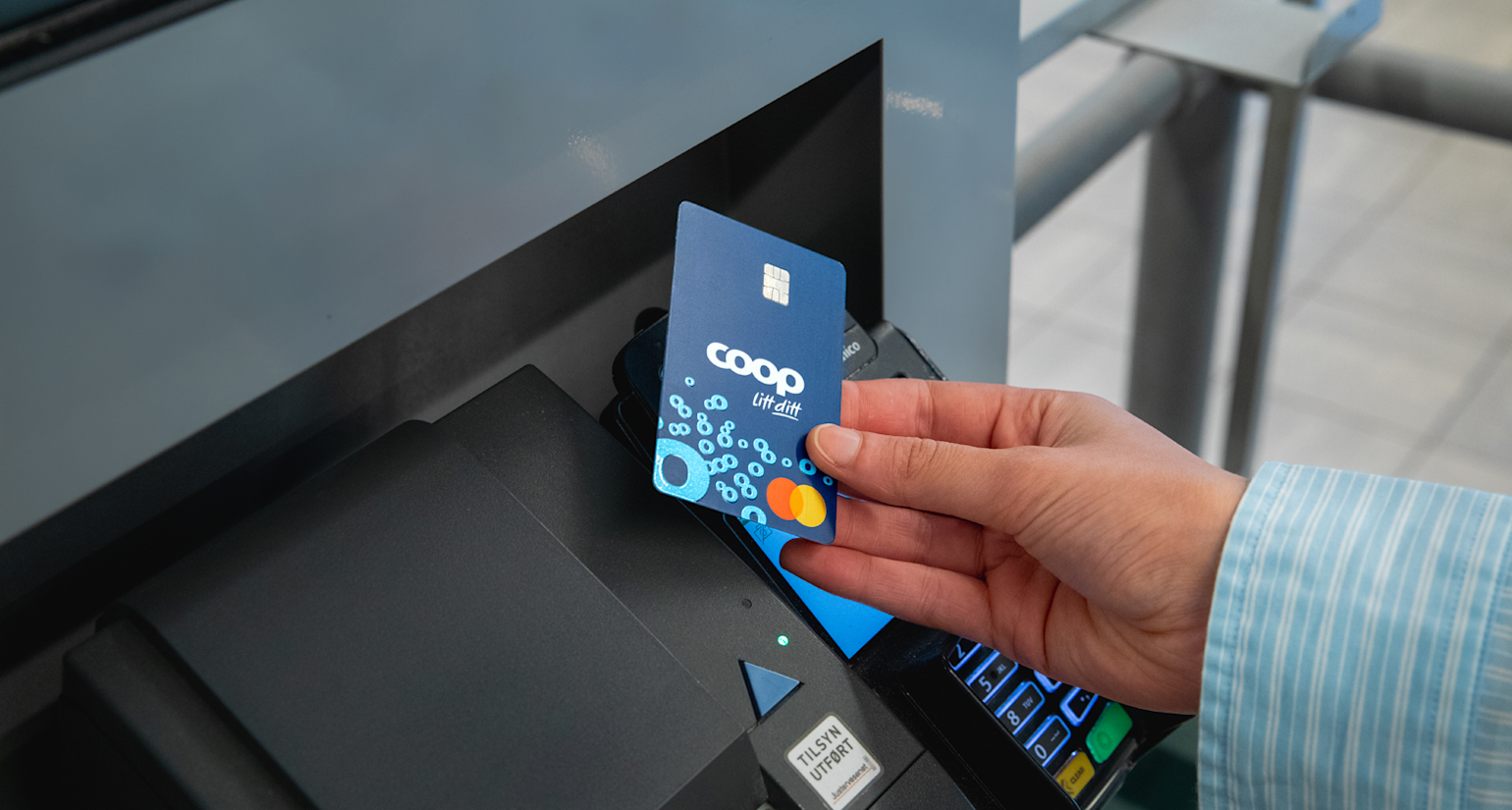 En hånd betaler i en kortterminal med Coop Mastercard