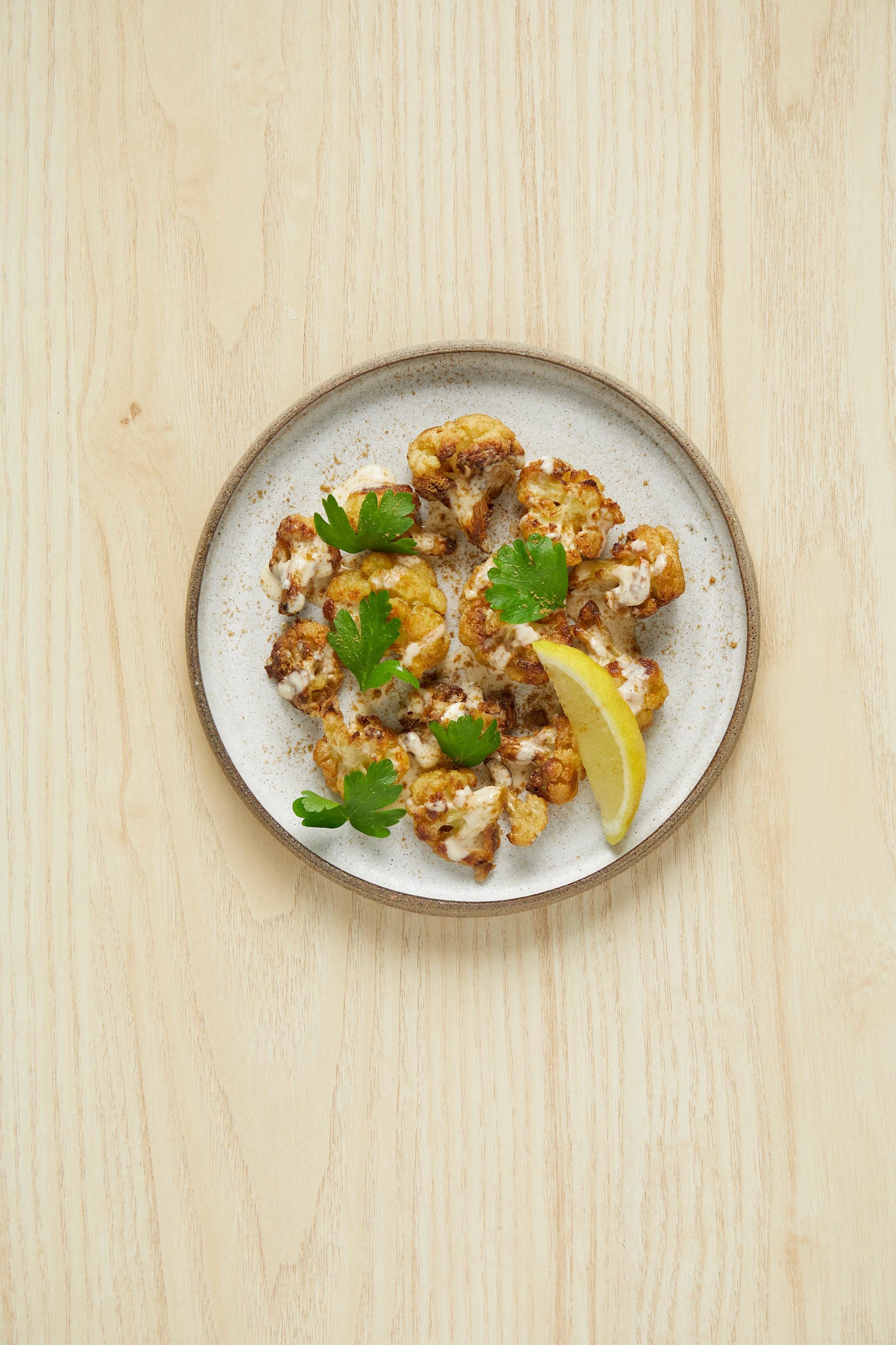 Sprø blomkålbiter - Libanesisk Arnabeet, servert på lys tallerken med friske urter og en sitronskive, på lyst trebord.
