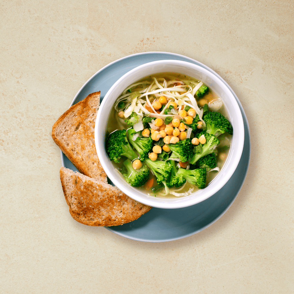 Grønnsakssuppe med kål, mais og brokkoli, i en hvit skål på en tallerken med en oppskjært brødskive