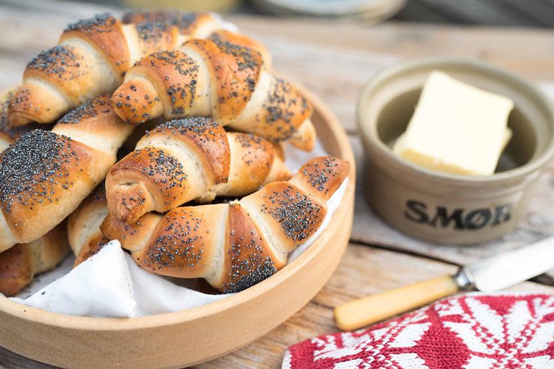 Hjemmebakte horn med valmuefrø, servert i trebolle på rustikk trebord. Smørtine med smør ved siden av.
