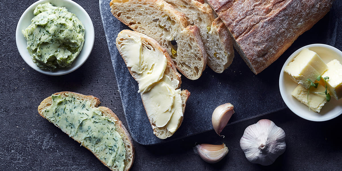 3 fantastiske kryddersmør, servert på brød og i skål. Mørk bakgrunn.