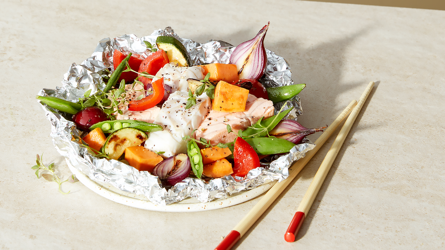 Hvit og rød fisk grillet i foliepakke, med fargerike grønnsaker. Lys bakgrunn.