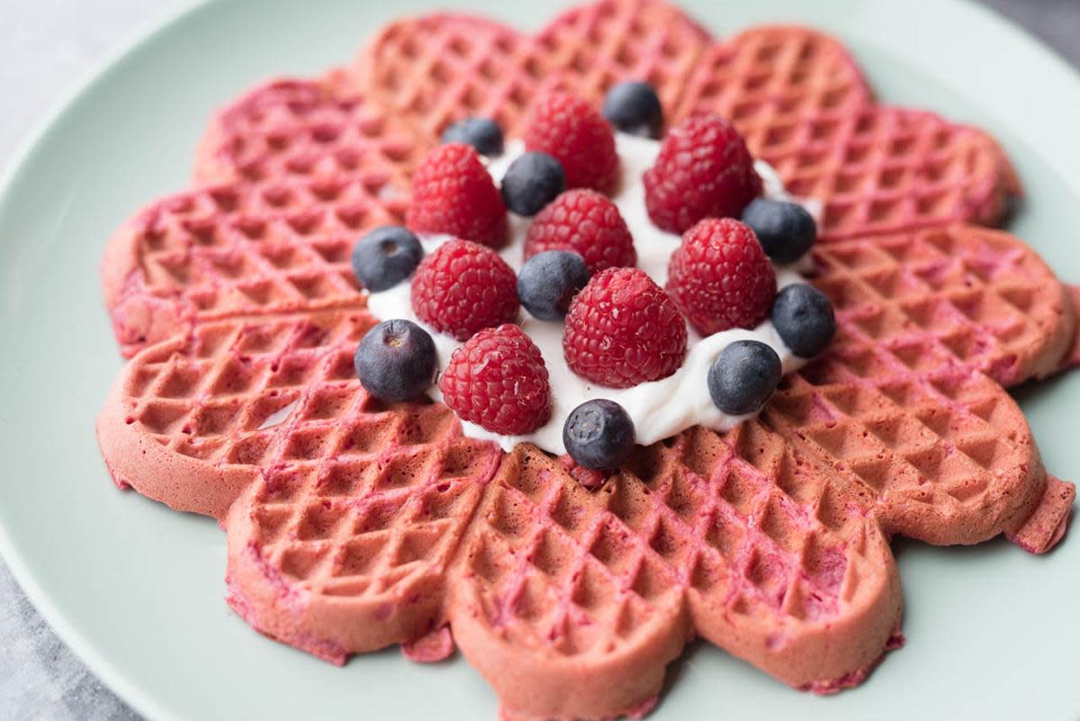 En rød vaffel laget med rødbeter, servert på lys tallerken med yoghurt, bringebær og blåbær.