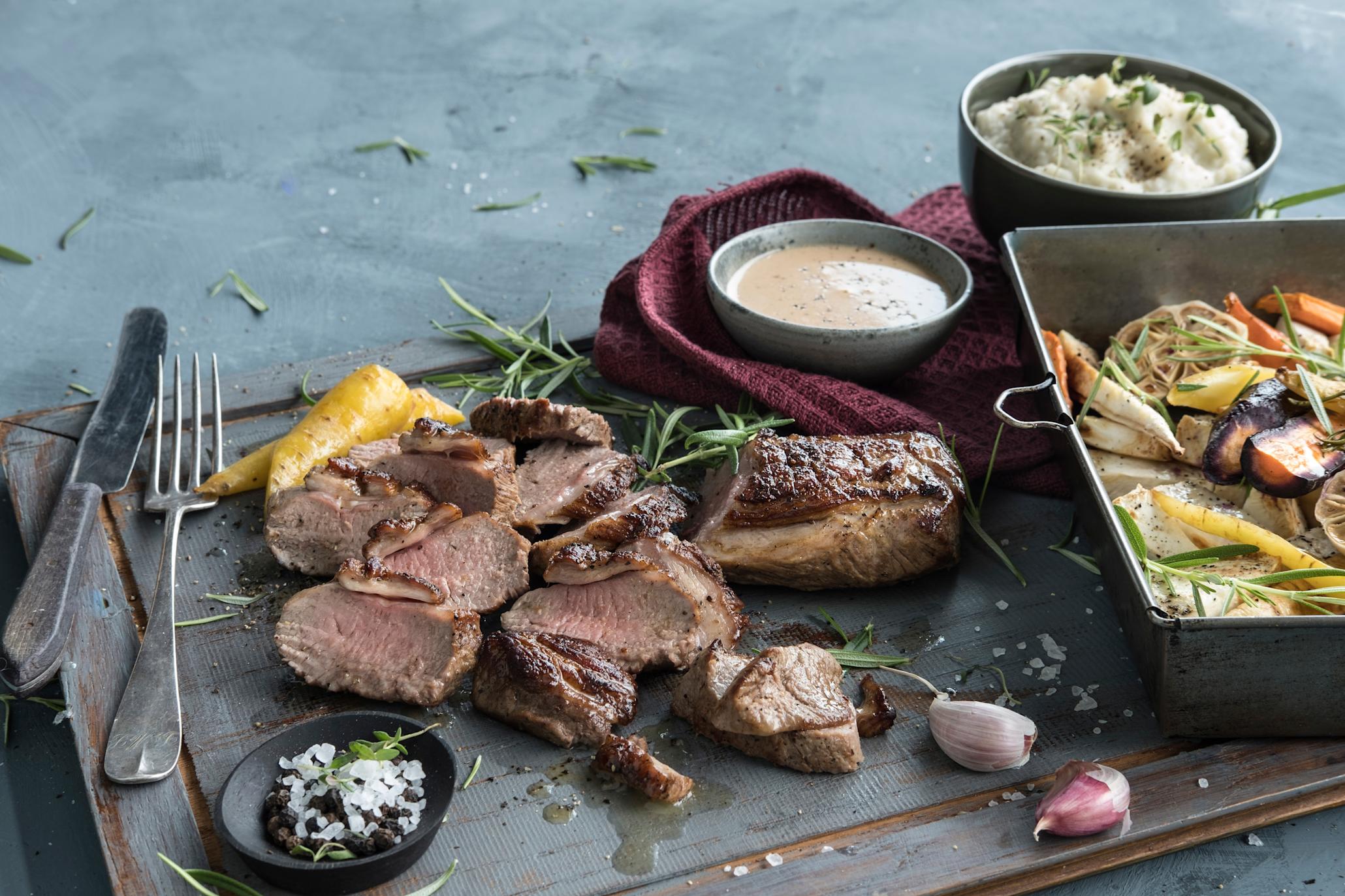 Ytrefilet av lam med ovnsbakte rotgrønnsaker, servert på rustikk trefjøl med jordskokkpure og lys saus.