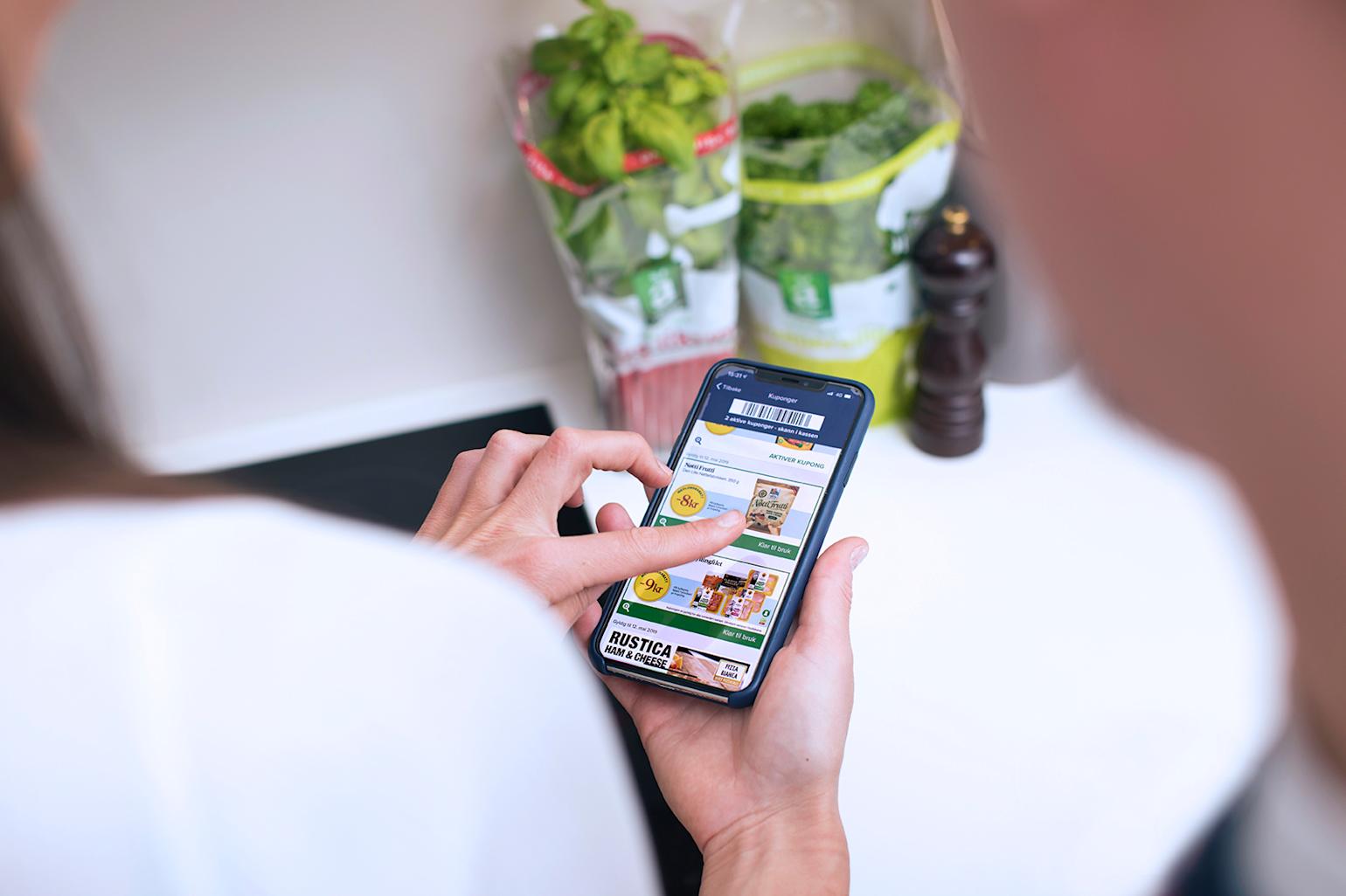 Kvinne scroller gjennom Coop kuponger på mobilen